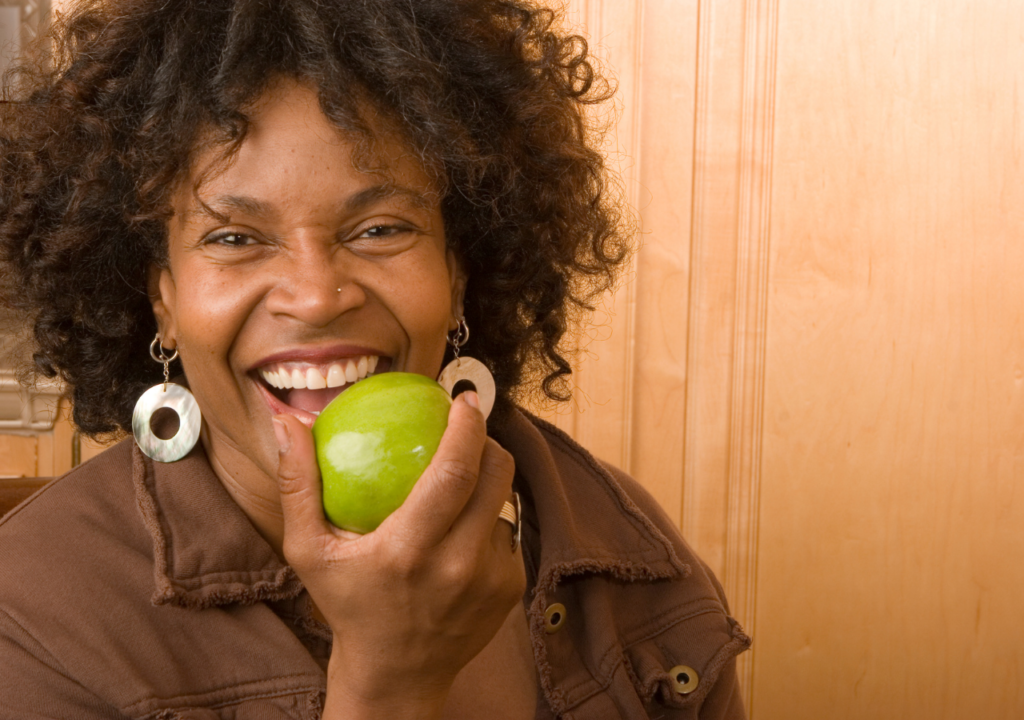 Black women smiling while eating a green apple
